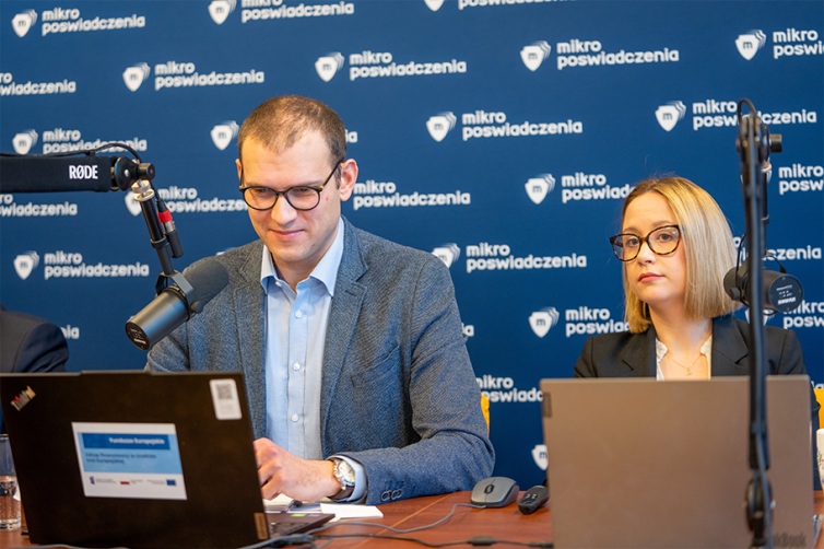 Grupa doradcza ds. Mikropoświadczeń - spotkanie. Dr Wojciech Gola i Martyna Leciejewicz, eksperci IBE, siedzą przy stole, przed sobą mają laptopy i mikrofony. Za nimi tło z logo projektu dotyczącego Mikropoświadczeń.